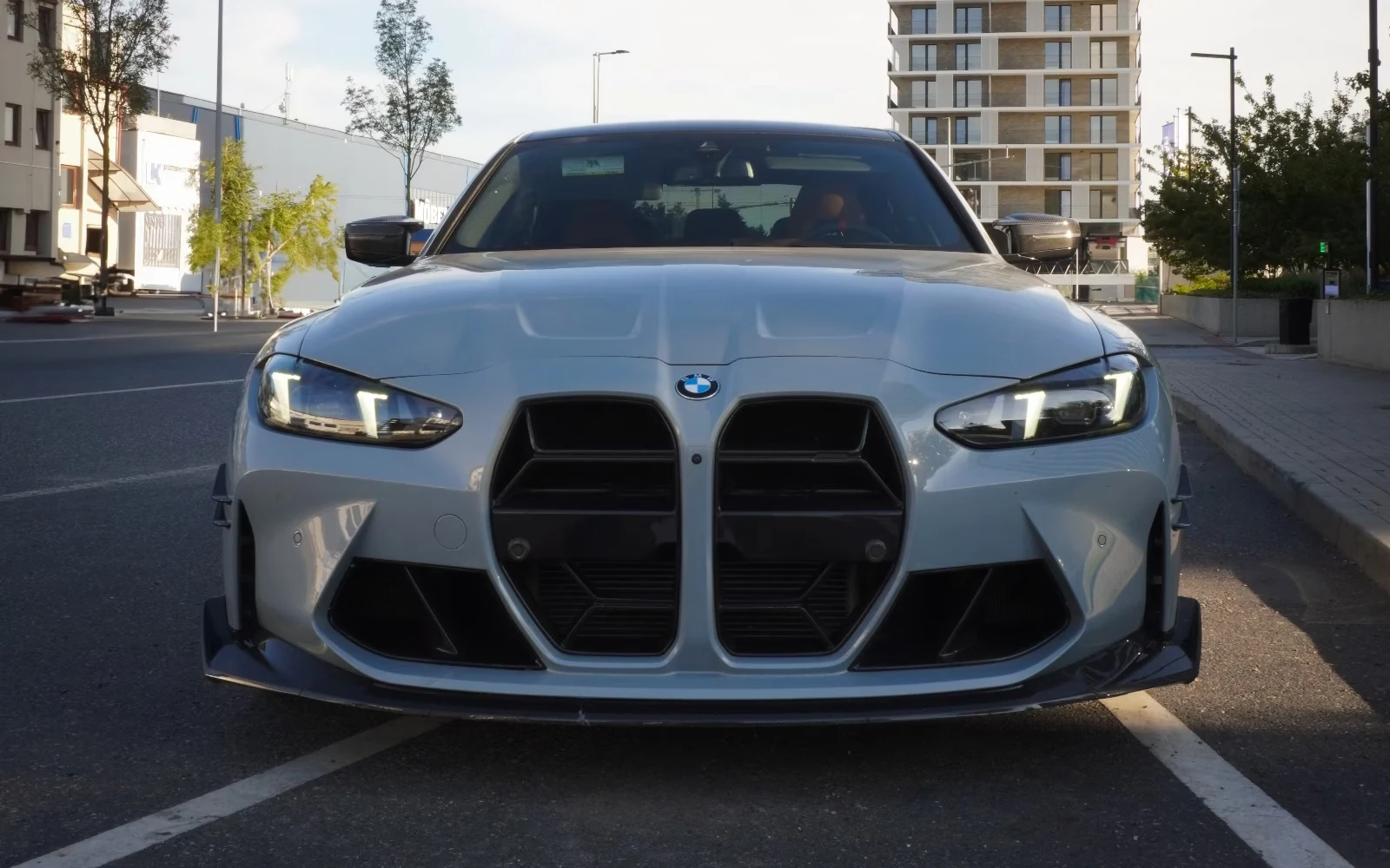 Šedé BMW M3 Competition zepředu s karbonovým splitterem zaparkované na ulici