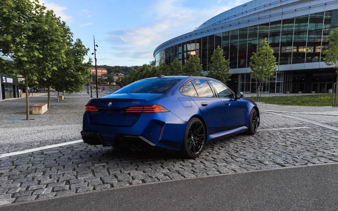 Modré BMW M5 zezadu z boku zaparkované u moderní architektury